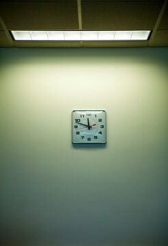 Clock on an office wall under a strip light, time nearly 11.50. Clockwatching.