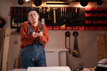 Woman joiner wears workwear in workshop scene with tools hanging on wall asking help with hands out...