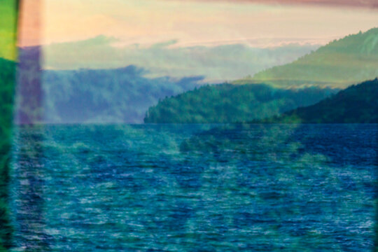 A reflection in window glass of the forest, mountains and moving water.