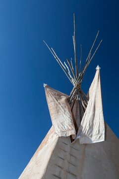 Close view of a traditional Plains tipi with canvas flaps and wooden poles reaching into a deep blue sky in the Black Hills of South Dakota.