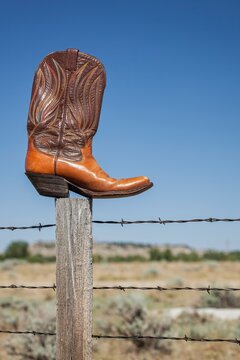 A single cowboy boot rests on a fence post against a clear blue sky in Wyoming. Symbol of the American West and cowboy heritage.