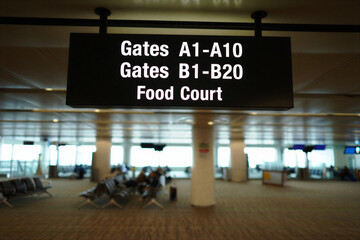 Airport terminal sign with gates and food court information in a travel hub interior with seating area