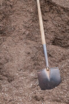 Metal shovel resting in a large pile of fertilizer at a commercial plant nursery in Oregon, symbolizing agriculture and gardening.