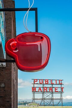 Red neon coffee cup sign glows beside the iconic Public Market sign at Pike Place Market in Seattle, Washington.