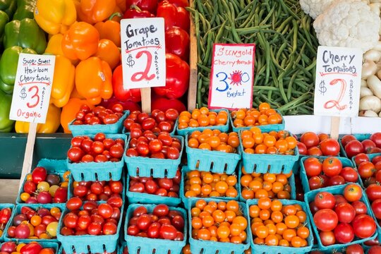 Colorful baskets of grape and cherry tomatoes displayed for sale alongside peppers, beans, and cauliflower at Pike Place Market in Seattle, Washington.