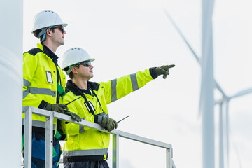 Two professional engineers in safety gear using walkie-talkies to communicate and coordinate during a technical inspection at a renewable energy wind farm.