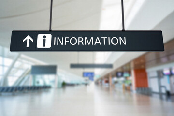Information sign with white arrow pointing up and letter i in a white square on black background in airport terminal hallway with blurry background