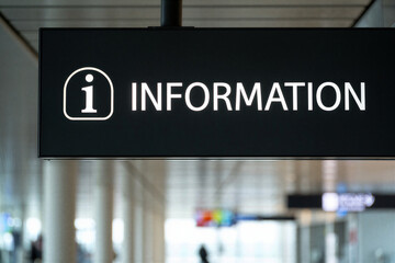 Information sign with white text and icon on black panel in blurred airport or train station interior with people and advertisements