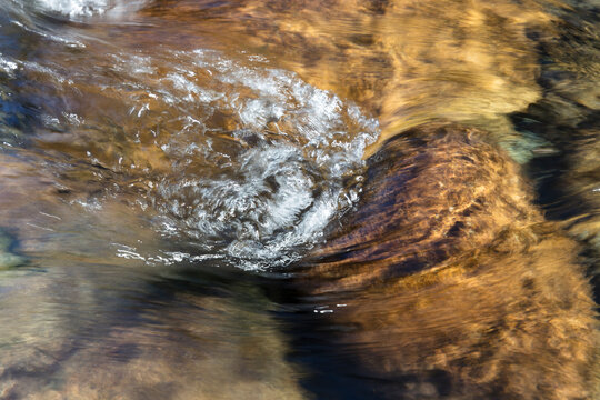 Long exposure of clear clean river water flowing over boulders and rocks