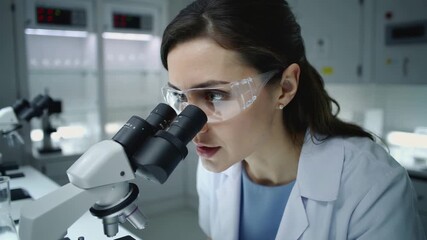 Female scientist conducting research with microscope in laboratory. Professional researcher analyzing samples in modern medical facility. Close-up shot with panning movement. - Powered by Adobe