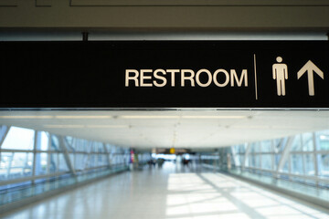 Restroom sign with arrow pointing up in a large modern interior space with glass walls and people walking  airport terminal hallway