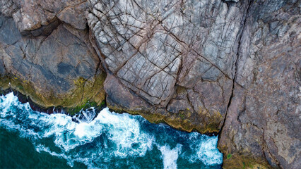 Aerial close-up view of ocean waves crashing against rocky tropical coastline in Brazil. Powerful sea and natural coastal textures.