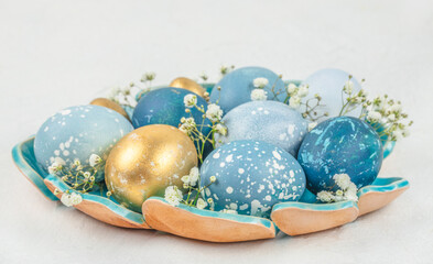 Stylish Easter eggs in ceramic bowl with blue and gold colors on white background