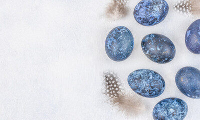 Blue Easter eggs with feathers on white textured background, top view with copy space for holiday branding. Top view