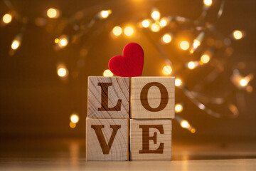 Wooden blocks spelling love with red heart on top and blurred fairy lights in background for valentines day or romance concept