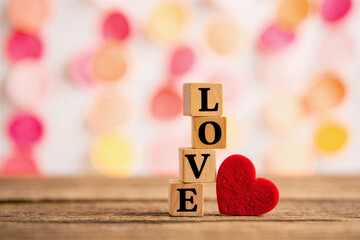 Wooden blocks spelling love with red heart on wooden table with colorful bokeh background