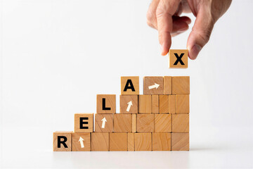 Wooden blocks stacked in a pyramid shape with a hand placing an X block on top of the word RELAX  relaxation concept