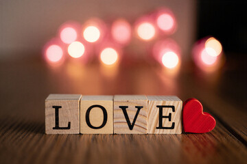 Wooden blocks with love text and red heart on wooden table with blurred bokeh lights in the background for valentines day