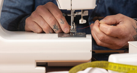 Craftsperson hands threading sewing machine needle with red thread