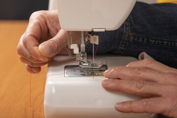 Hands threading red yarn into sewing machine needle