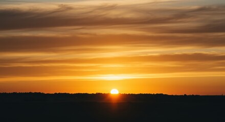 Vibrant orange and yellow hues illuminate streaked clouds during an intense evening descent over a distant horizon.