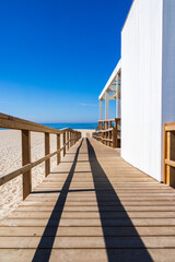 Wooden boardwalk leading toward Atlantic Ocean and sandy beach under clear blue sky in Torreira...