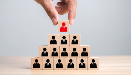 Hand placing a red leader icon at the top of a wooden block pyramid symbolizing corporate hierarchy and leadership
