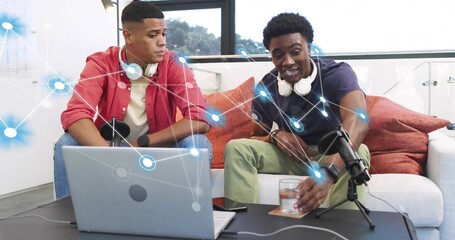Recording two men in red shirt and navy polo speaking into microphone in living-room studio, laptop