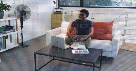 Playing man in dark tee, olive pants holding controller with laptop in living room, copy space