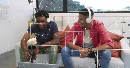 Recording two podcasters wearing navy tee and red shirt with headphones on sofa, mics and laptop