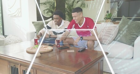 Leaning, two men reaching for pizza on living room sofa, wearing red jersey and beige shirt