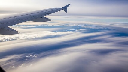 Airplane wing above a vast expanse of clouds and blue sky during a high-altitude flight.