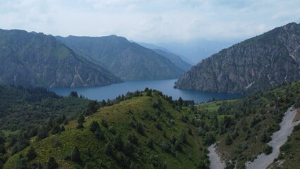 Aerial view of a turquoise mountain lake surrounded by rugged terrain. Clear water contrasting with rocky landscape, photographed from a drone.