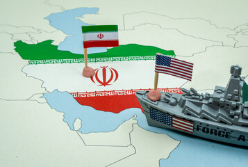 United States and Iran national flags on a geopolitical map with a toy warship, representing a potential military conflict or diplomatic tension between the two countries © tanaonte