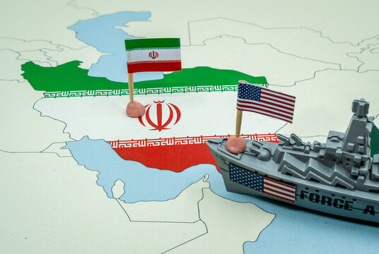United States and Iran national flags on a geopolitical map with a toy warship, representing a potential military conflict or diplomatic tension between the two countries