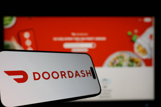 Kiel, Germany - 01-12-2026: Smartphone displaying DoorDash logo in front of the company website on a monitor