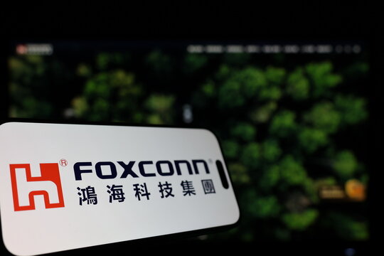 Kiel, Germany - 01-12-2026: Smartphone displaying Foxconn logo in front of the company website on a monitor