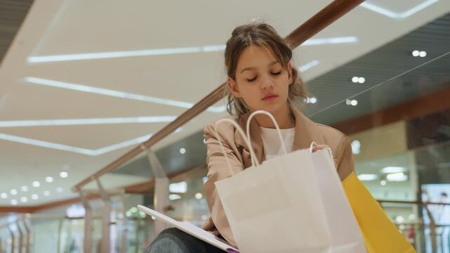 young caucasian woman searching inside shopping bag for coupon or phone, focused hands rummaging through purchases, mall lights and boutiques in background, casual blazer and attentive mood