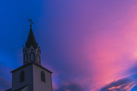 View of a church steeple piercing the vibrant twilight sky, painted with hues of pink and purple against the deepening blue, Saudarkrokur, Skagafjordur, Iceland.