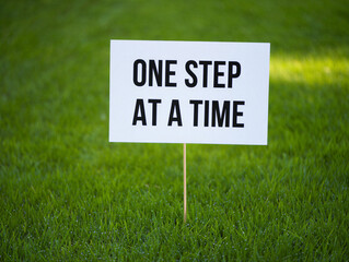 A white yard sign on a wooden stake with a motivational quote on green grass lawn  outdoor inspirational message