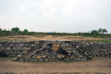 View of ancient stone walls and grassy mounds under a pale sky, hinting at stories etched in time, Taxila, Punjab, Pakistan.