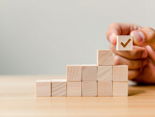 Hand holding wooden block with check mark above stack of blocks on light wood table and gray background