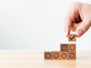 Hand placing wooden block with check mark on top of stacked blocks on a table