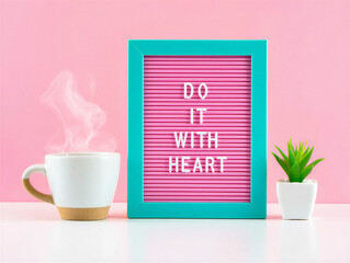 Inspirational quote on pink board with teal frame and steaming coffee cup on white table against pink wall with small plant