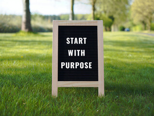 Inspirational quote sign start with purpose on grass with trees in background  motivational message board outdoors