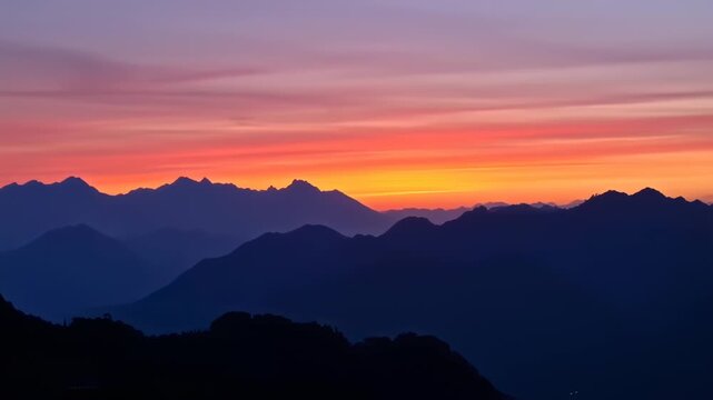 Majestic mountain silhouettes under a vibrant sunset sky. Colors range from deep blue to fiery orange