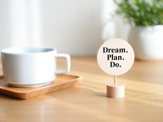 White coffee mug on wooden tray and small wooden stand with inspirational motivational quote Dream Plan Do on light wood table