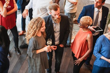 Diverse group at a social event, mingling and chatting. People enjoying drinks, socializing, and...