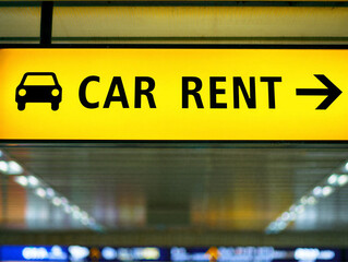 Yellow car rent sign with black text and arrow pointing to the right in an airport or travel terminal setting