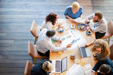 Group of professionals in a meeting, discussing graphs. Teamwork and collaboration around a table with laptops and coffee. Business meeting setting. Business team planning and working on project.